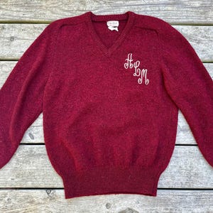 May include: A maroon v-neck sweater with long sleeves and embroidered initials "HLM" on the front.