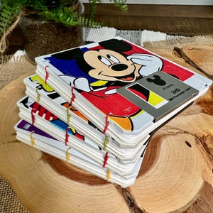 May include: A stack of five colourful notebooks with a Mickey Mouse design on the front cover. The cover features a red, yellow and black Mickey Mouse with the text "Disney 2HD 1hr Formatted Album".