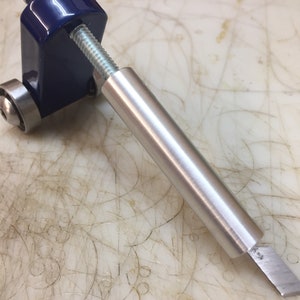 May include: A metal edge tool with a blue body, silver screw, and a silver blade. The tool has a cylindrical handle and is designed for precision work. The blade is angled and appears sharp. The tool is designed for leathercraft or similar crafts.