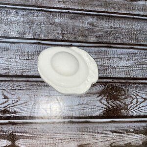 May include: A white ceramic egg-shaped dish with a slightly irregular edge. The dish has a smooth, glossy surface and a shallow, rounded center. The design mimics a fried egg, perfect for serving small portions or as a decorative accent.