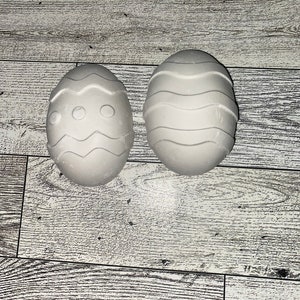 May include: Two white ceramic Easter eggs, one with a wavy pattern and the other with a wavy pattern and three circles.