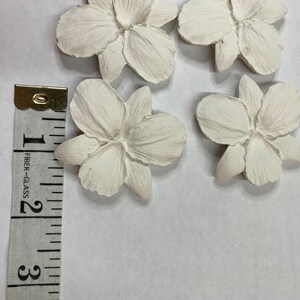May include: Four off-white, flower-shaped decorative pieces. Each flower has five petals and a textured surface. A measuring tape shows the flowers are approximately 2 inches in diameter.