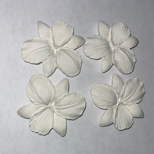 May include: Four white, flower-shaped decorative elements. Each flower has multiple petals and a detailed, textured surface. The objects are arranged on a white background, showcasing their delicate design and potential for craft projects.