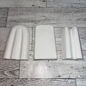 May include: Three white popsicle molds, two with a ribbed design and one smooth, on a woodgrain surface.