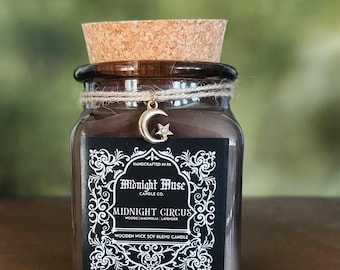 May include: A brown glass jar candle with a cork stopper and a decorative charm. The label reads "Midnight Circus" and "Wooden Wick Soy Blend Candle". The candle is handcrafted and features a moon and star charm.