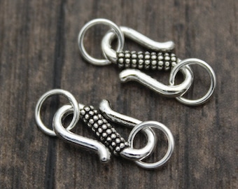 May include: Two silver-toned metal clasps with a textured design. Each clasp has a round ring on one end and a hook on the other end.