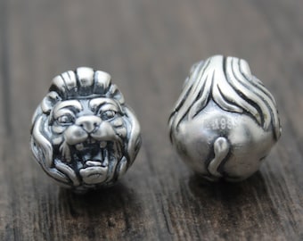 May include: A silver charm bead with a detailed lion head on one side and a lion tail on the other side.