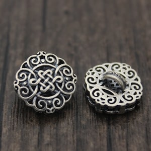 May include: Two silver-toned decorative buttons with an intricate, Celtic-inspired design. One button has a loop on the back for sewing.