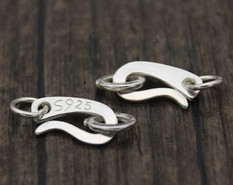 May include: Two silver-colored jewelry clasps with a curved design and small rings. One clasp has the number "5925" engraved on it. The clasps are on a dark wood surface.