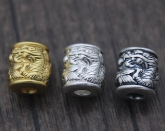 May include: Three cylindrical beads with a dragon design. The beads are made of metal and are gold, silver, and black in color.
