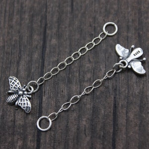 Peut inclure: Deux chaînes en argent avec des breloques en forme d'abeille et de papillon. Les chaînes sont reliées par des anneaux de jonction. Le charme d'abeille a un design détaillé et le charme de papillon a un poinçon 925.