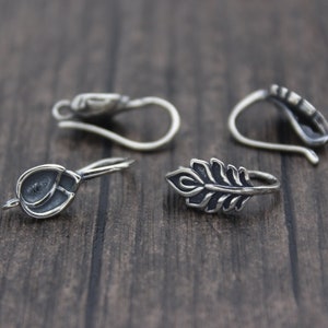 May include: Four silver earring hooks with different designs. Two hooks have a simple round shape, one has a leaf design, and one has a more intricate design.