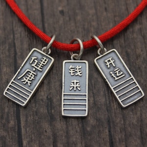 May include: A red string necklace with three silver charms. Each charm has a different Chinese character written on it. The characters are "Order", "Come", and "Open".
