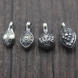 May include: Four silver pendant charms with intricate designs. The charms are in the shape of a teardrop, a circle, a heart, and a leaf. The charms are all silver and have a shiny finish.