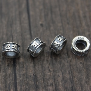 May include: Four silver rings with engraved characters. The rings are on a wooden surface.