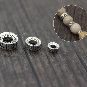 May include: Three silver metal beads with engraved designs. The beads are different sizes and are arranged in order of size from left to right.