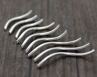 May include: A set of eight silver-toned wavy metal beads. The beads are all the same size and shape, and they are arranged in a row.