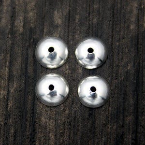 May include: Four silver-colored metal bead caps, arranged in a square pattern on a dark wood surface.