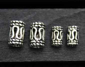 May include: Four silver metal beads with intricate designs. The beads are different sizes and are arranged in a row on a dark wooden surface.
