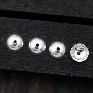 May include: Five silver metal beads with a hole in the center, arranged in a row on a dark wooden surface.