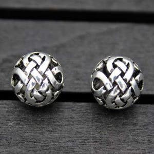 Op de afbeelding: Twee zilverkleurige metalen kralen met een ingewikkeld knoopontwerp.