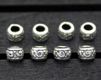 May include: Eight silver-toned metal beads with an intricate design. The beads are arranged in two rows of four on a dark wooden surface.