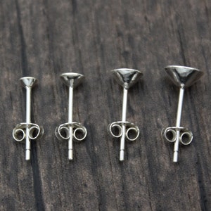 May include: Four silver earring posts of different sizes, shown from the back. The posts are all made of metal and have a simple design.