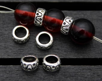 May include: A close-up of a string of red and black glass beads with silver spacer beads. The beads are on a black surface.