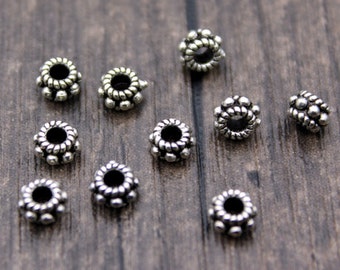 May include: A group of silver-toned metal bead caps with a decorative design. The bead caps are arranged in a circular pattern on a wooden surface.