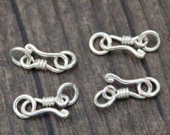 May include: Four silver-toned metal clasps with a twisted wire design. The clasps are designed to be used for jewelry making.