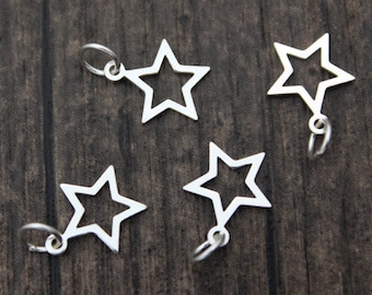 May include: Four silver star-shaped charms with a loop at the top. The charms are arranged on a dark wood surface.