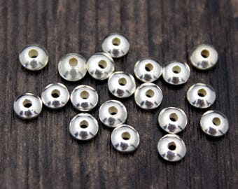 May include: A group of silver-toned metal beads, each with a flat, circular top and a small hole in the center. The beads are scattered on a dark wooden surface.