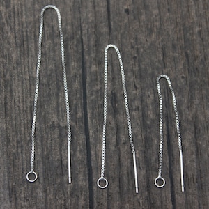 May include: Three pairs of silver chain earrings with a small circle at the top and a straight metal bar at the bottom. The earrings are arranged in order of length, with the longest pair on the left and the shortest pair on the right.