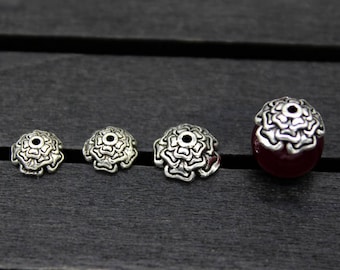 May include: Four silver metal flower-shaped bead caps with a center hole, and one larger silver metal flower-shaped bead cap with a red stone center.