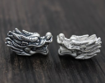 May include: Two silver dragon head charms, each with intricate details and a textured finish. The charms are facing each other, with their mouths slightly open.