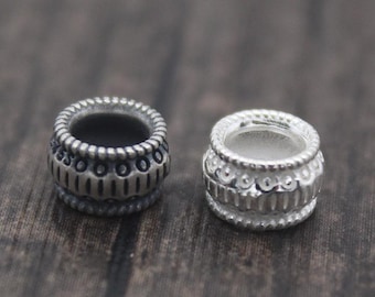 May include: Two silver bead spacers, one with a black oxidized finish and one with a polished silver finish. Both beads have a decorative pattern.
