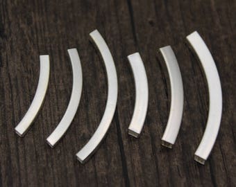 May include: Six silver metal curved pieces, each with a slightly different size and shape, arranged in a row on a dark wood surface.