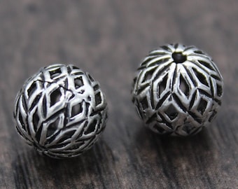 May include: Two silver metal beads with a geometric design. The beads are round and have a hollow center.