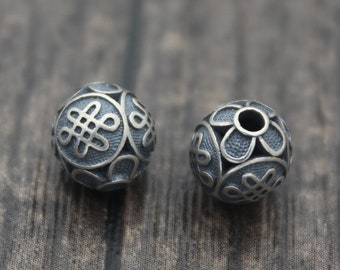 May include: Two silver beads with intricate knot designs. The beads are round and have a hole in the center for stringing.