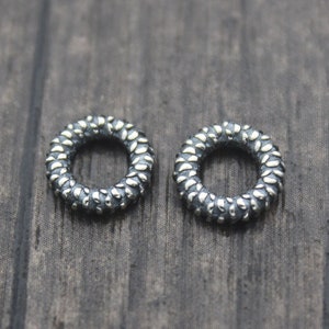 May include: Two silver rings with a textured surface. The rings are round and have a small opening in the center.
