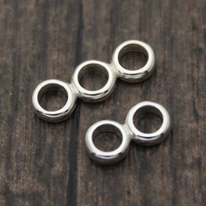 Puede incluir: Dos piezas de conexión de metal plateado para la elaboración de joyas. Cada pieza tiene tres o dos anillos conectados.