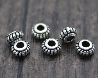 May include: Six silver metal beads with a decorative design. The beads have a round shape with a hole in the center.