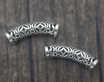 May include: Two silver metal bead caps with an intricate geometric design. The caps are curved and have a smooth, polished finish.