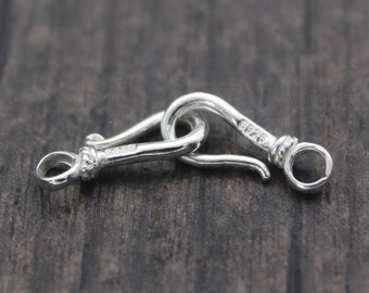 May include: Silver clasp with a hook and loop design. The clasp is made of polished silver and has a smooth finish.