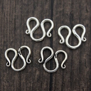 May include: Four silver-toned lobster clasps, each with a double loop design, are arranged on a dark wood surface.