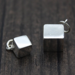 Può includere: Due ciondoli a forma di cubo d'argento con un anello per attaccarli a una collana o un braccialetto. I ciondoli sono di dimensioni diverse.