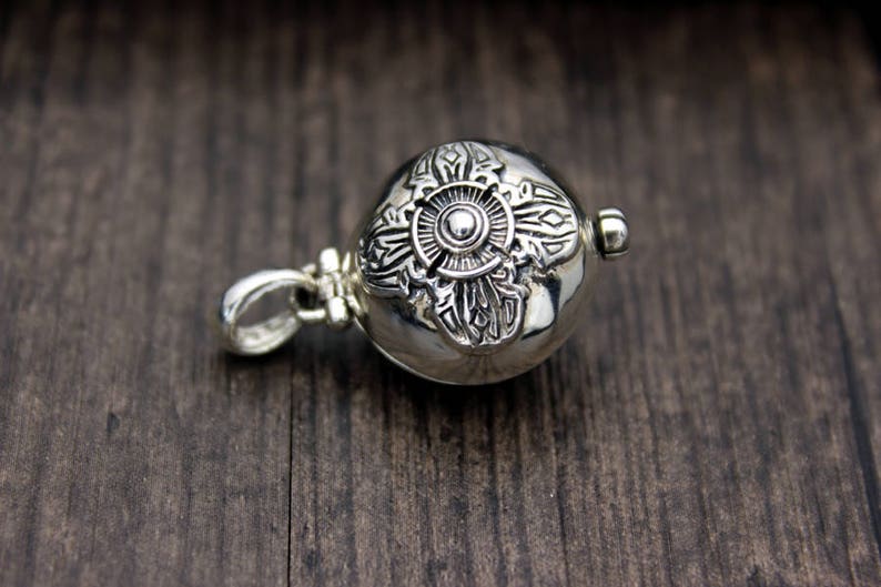 May include: A silver charm with an intricate design, featuring a circular center with a smaller circle inside. The charm has a loop for attaching to a necklace or bracelet.