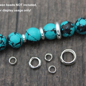 May include: A turquoise and black gemstone bracelet with silver spacer beads. The bracelet is shown with five silver jump rings of varying sizes.