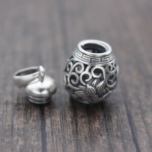 Puede incluir: Un charm de plata en forma de peque&ntilde;o frasco redondo adornado con tapa. El frasco tiene un dise&ntilde;o floral y est&aacute; abierto en la parte superior. La tapa est&aacute; separada y tiene un bucle para sujetarlo a una cadena.