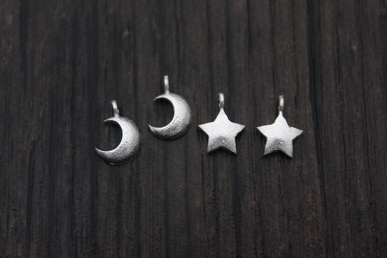 May include: Five silver charms, two crescent moons and three five-pointed stars, on a dark wood background.